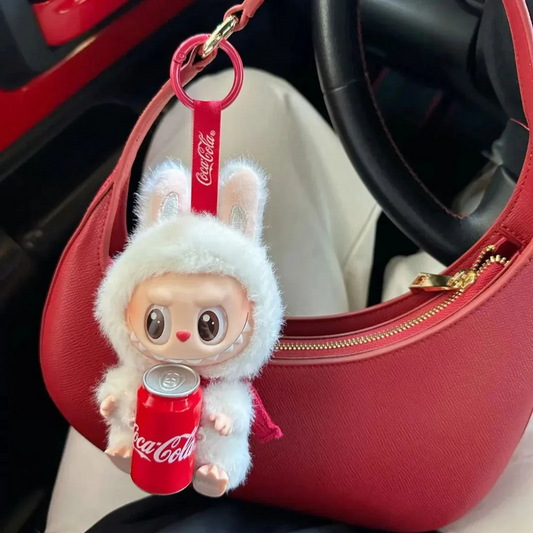Coca-Cola bunny keychain doll with mini soda can on red handbag in car interior